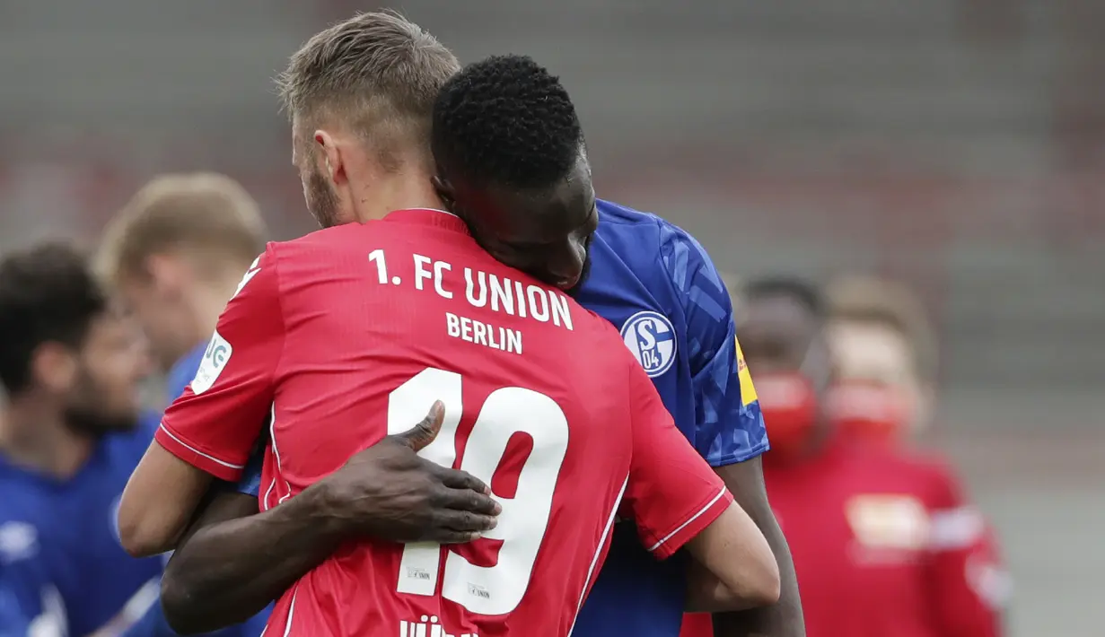 Pemain Union Berlin, Florian Huebner, berpelukan dengan pemain Schalke, Salif Sane, pada laga Bundesliga di Weserstadion Minggu (7/6/2020). Kedua tim bermain imbang 1-1. (AP/Michael Sohn)