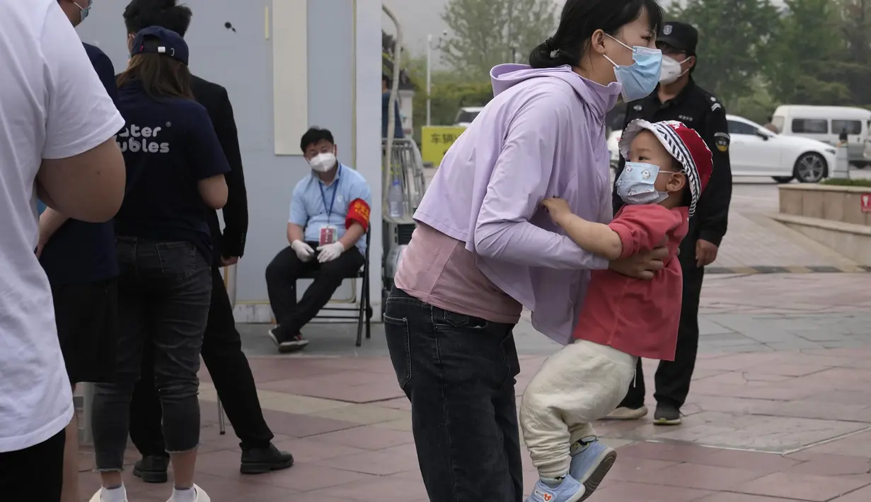 <p>Seorang wanita menggendong seorang anak di dekat garis selama pengujian massal untuk COVID-19 di distrik Chaoyang, Bejing, Senin (25/4/2022). Ibu kota China, Beijing, mulai menguji jutaan penduduk dan menutup kawasan perumahan dan bisnis pada Senin di tengah wabah baru COVID-19. (AP Photo/Ng Han Guan)</p>