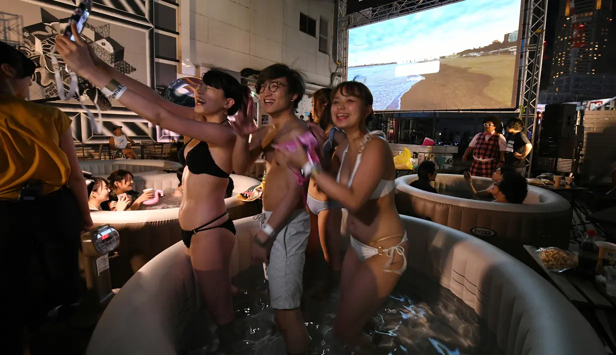 Pengunjung menonton film sambil berendam di Bathtub Cinema di atap gedung kawasan Shibuya, Tokyo, 17 Agustus 2018. Event musim panas ersebut merupakan acara menonton dalam bathtub yang pertama kali hadir di Negeri Matahari Terbit itu.  (AFP/Kazuhiro NOGI)