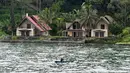 Nelayan mendayung melewati penginapan bernuansa resort di Pulau Samosir, di tengah Danau Toba, Sumatra Utara, 3 April 2019. Danau berkawah seluas 1.145 kilometer persegi ini diperkirakan terbentuk dari letusan supervolcano Gunung Toba yang terjadi sekitar 74.000 tahun lalu. (GOH CHAI HIN / AFP)