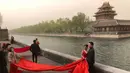 Pasangan pengantin berpose untuk foto di dekat Kota Terlarang saat badai pasir di Beijing (28/3/2021). Badai pasir kembali menyapu Beijing pada Minggu (28/3), mengubah langit menjadi kuning, membatasi jarak pandang dan mengganggu lalu lintas. (AP Photo/Ng Han Guan)