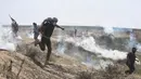 Warga Palestina berlindung dari tembakkan gas air mata pasukan Israel di perbatasan Jalur Gaza dengan Israel, (6/4). Aksi ini bertujuan untuk merebut kembali tanah kelahiran mereka yang direnggut Israel tujuh dekade silam. (AP Photo/Khalil Hamra)