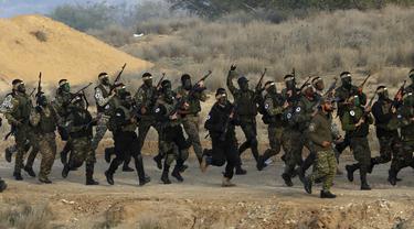 Militan Palestina dengan wajah dicat berbaris dengan senjata mereka dan meneriakkan slogan-slogan selama latihan militer yang diselenggarakan oleh faksi-faksi militer di Rafah, Jalur Gaza selatan, Rabu (29/12/2021). (AP Photo/Adel Hana)
