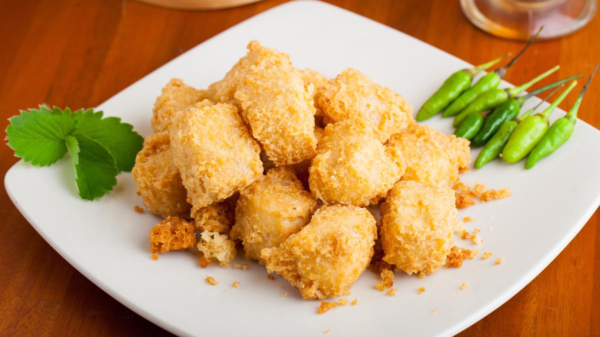 Tahu goreng tepung berwarna keemasan dengan lapisan crispy yang menggoda, disajikan bersama irisan daun bawang segar dan saus sambal