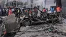 Tim penyelamat dan pengamat berkumpul di dekat puing-puing di lokasi serangan bom mobil bunuh diri di dekat pos pemeriksaan keamanan di Mogadishu, Somalia (13/2/2021). Rentetan tembakan juga berulang kali terdengar setelah ledakan di saat jam sibuk tersebut. (Abdirazak Hussein FARAH / AFP)