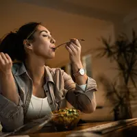 Seorang perempuan sedang menikmati makanannya di meja makan (Foto Dok: Freepik/Drazen Zigic).