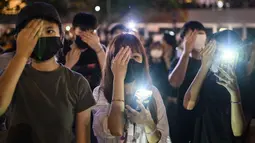 Mahasiswa menutup mata kanan mereka sambil menyalakan ponselnya selama rapat umum di Hong Kong (22/8/2019). para mahasiswa masih ingin memimpin barisan demonstran pro-demokrasi yang hampir setiap hari berada di jalanan untuk memberikan tekanan pada pemerintah. (AFP Photo/Anthony Wallace)