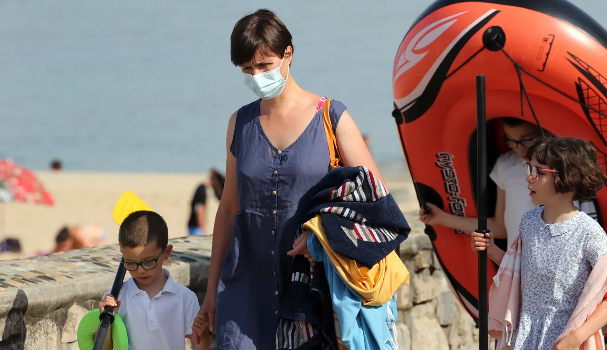 Seorang wanita mengenakan masker berjalan dengan anak-anaknya di sepanjang pantai di Saint Jean de Luz, Prancis barat daya, Selasa (27/7/2021). Otoritas setempat di Prancis memberlakukan kembali mandat masker karena penyebaran varian delta menyebabkan rawat inap meningkat lagi. (AP/Bob Edme)