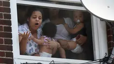 Wanita menggendong bayi menunggu bantuan setelah kebakaran terjadi di dalam gedung apartemen di Hazleton, Pennsylvania (26/7/2019). Pemadam kebakaran kota menggunakan truk menyelamatkan penghuni dari lantai tiga gedung. (Warren Ruda/Hazleton Standard-Speaker via AP)