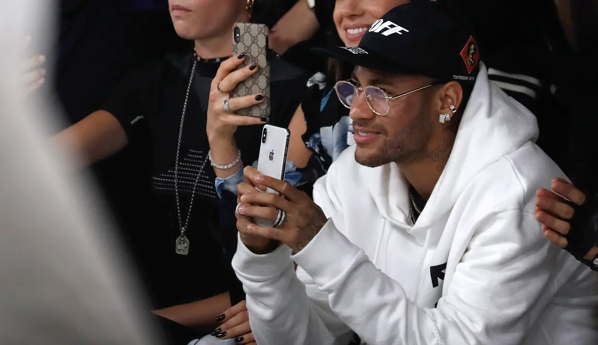 Pemain PSG, Neymar bermain ponsel saat menghadiri acara peragaan busana Off-White Spring-Summer 2019 Ready-to-Wear selama Paris Fashion Week, Prancis (27/9). Neymar tampil mengenakan jaket putih dan kaca mata emas. (AFP Photo/Francois Guillot)