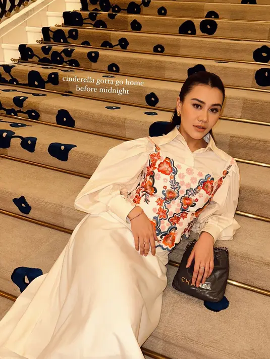 Outfit putih polos itu dipadukan dengan korset bunga-bunga yang vibrant dan tas Chanel abu-abu [@aaliyah.massaid]