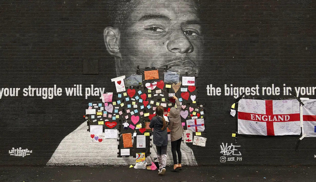 Orang-orang menempatkan pesan dukungan di atas bin liner yang ditempel di atas kata-kata ofensif di mural striker Inggris Marcus Rashford di dinding Coffee House Cafe, yang dirusak pagi hari setelah Inggris kalah di final Euro 2021 melawan Italia, di Manchester (12/7/2021). (Peter Byrne/PA via AP)