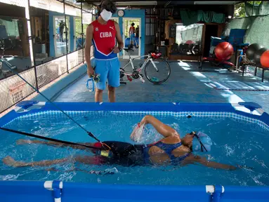 Leslie Amat, seorang atlet triathlon Kuba, berenang di kolam kecil di bawah pengawasan pelatihnya Dioseles Fernandez di teras rumahnya di Havana, Senin (20/4/2020). Atlet Kuba tak bisa berlatih di fasilitas olahraga seperti biasanya selama pademi corona. (AP /Ismael Francisco)