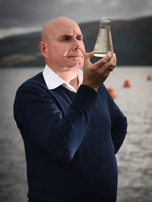 Ahli genetika Universitas Otago Profesor Neil Gemmell berpose dengan wadah air di perairan Loch Ness, Drumnadrochit, Skotlandia, Kamis (5/9/2019). Ilmuwan yang meneliti keberadaan moster legendaris Loch Ness menemukan bahwa DNA dari belut sangat melimpah di perairan itu. (Andy Buchanan/AFP)