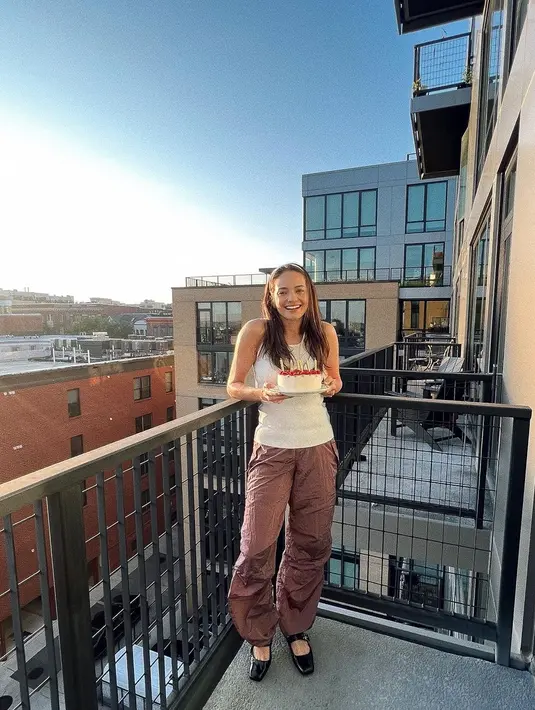 <p>Penampilan sederhana Enzy Storia merayakan ulang tahunnya setelah pindah ke Amerika. Ia tampak berpose membawa kue ulang tahun mengenakan tank top putih, dengan celana parasut cokelat. [Foto: Instagram/enzystoria]</p>