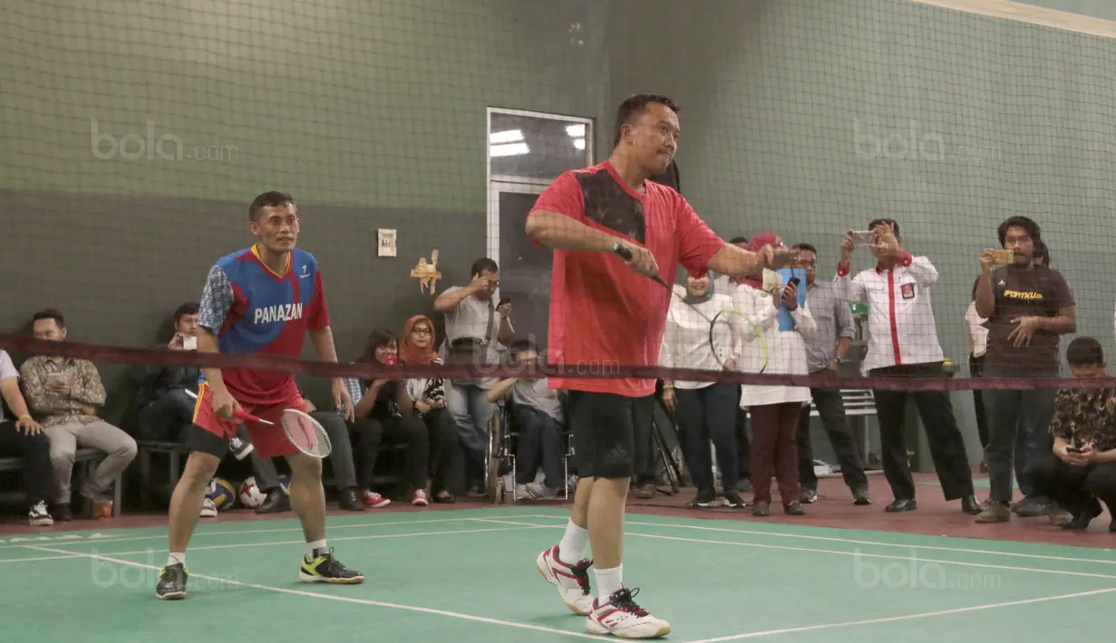 Aksi Menpora, Imam Nahrawi melakukan servis ke arah Kevin Sanjaya dan Marcus Gideon pada laga eksebisi bulutangkis di Gedung Kemenpora, Senayan, Jakarta, (28/11/2017). Kevin-Marcus menang 21-13, 16-21 dan 27-25.(Bola.com/Nicklas Hanoatubun)