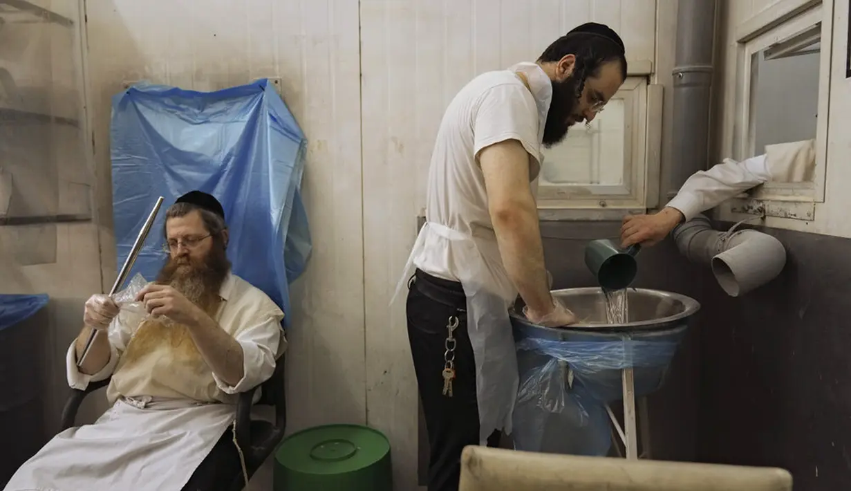 Yahudi Ultra-Ortodoks menyiapkan matzoh khusus di sebuah toko roti di Ashdod, Israel, 11 April 2022. Orang Yahudi dilarang makan makanan beragi selama liburan Paskah merayakan kisah alkitabiah tentang bangsa Israel saat melarikan diri dari perbudakan dan eksodus dari Mesir. (AP Photo/Tsafrir Abayov)