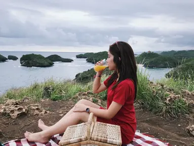 Fay Nabila tampak cantik dengan busana berwarna merah. Berpose di Pantai Kasap yang merupakan Raja Ampatnya Pacitan layaknya sedang piknik, ia tampak sedang minum jeruk dan menikmati indahnya suasana pantai tersebut. (Liputan6.com/IG/faynabilalxndr)