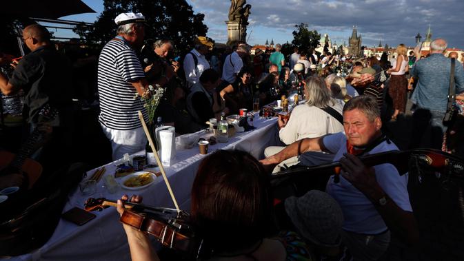 Warga memainkan musik saat makan malam bersama di atas meja sepanjang 500 meter di Charles Bridge di Praha, Republik Ceko, Selasa (30/6/2020). Kegiatan itu merupakan perpisahan simbolis yang digelar untuk menandai akhir dari masa krisis virus corona Covid-19 di negara tersebut. (AP/Petr David Josek)