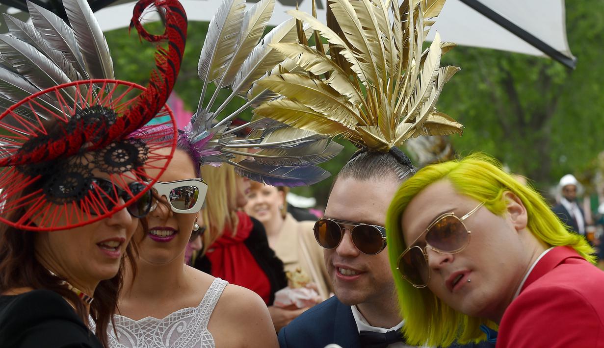 Para Racegoers berpose menggunakan hiasan kepala dan menggunakan gaun mewah yang saat menghadiri balap kuda Melbourne di arena pacuan kuda Flemington Racecourse di Melbourne, Australia (1/11). (AFP/Paul Crock)