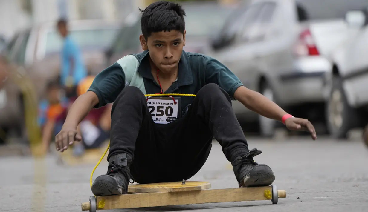 Seorang anak berpartisipasi dalam perlombaan jalanan tradisional "carruchas", sebutan untuk mobil kayu darurat di Caracas, Venezuela, Sabtu (18/12/2021). Anak-anak menikmati perlombaan yang menandai 10 tahun melestarikan tradisi ini. (AP Photo/Ariana Cubillos)