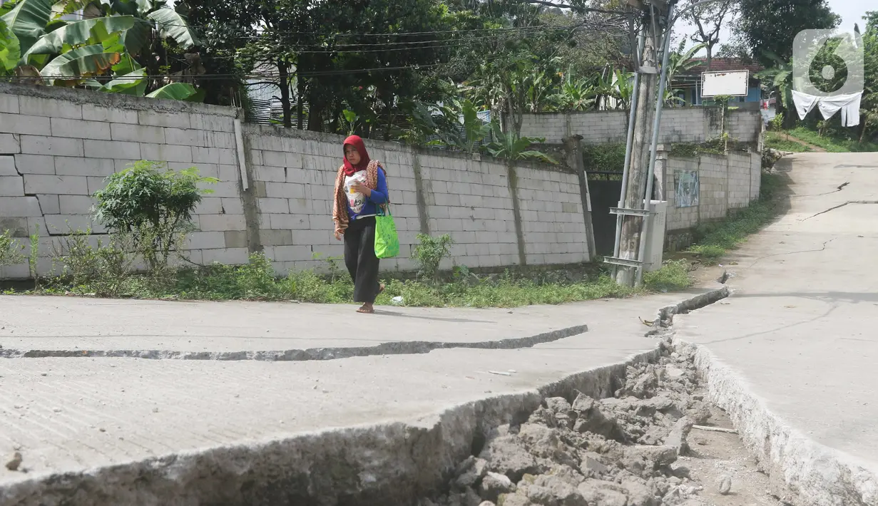 Seorang warga melintasi jalan yang terbelah akibat pergeseran tanah di kawasan Bojong Koneng, Babakan Madang, Kabupaten Bogor, Jawa Barat, Jumat (16/9/2022). Badan Penanggulangan Bencana Daerah (BPBD) setempat mencatat 18 unit rumah mengalami kerusakan, dan pergeseran tanah itu menyebabkan retakan-retakan di tanah, dinding, plafon dan lantai rumah warga serta akses jalan sudah tidak bisa dilewati oleh kendaraan roda dua dan roda empat. (Liputan6.com/Herman Zakharia)