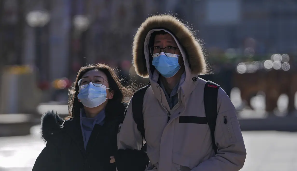 Sepasang suami istri mengenakan masker untuk membantu mengekang penyebaran virus corona berjalan melalui distrik perbelanjaan Wangfujing di Beijing, Minggu (12/12/2021).  (AP Photo/Andy Wong)
