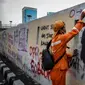 Petugas PPSU membersihkan coretan yang mengotori pembatas jalan pascaunjuk rasa di kawasan DPR/MPR, Jakarta, Jumat (17/7/2020). Coretan tersebut dilakukan oleh massa yang menolak RUU Omnibus Law Cipta Lapangan Kerja di depan Gedung DPR pada Kamis (16/7) kemarin. (Liputan6.com/Faizal Fanani)