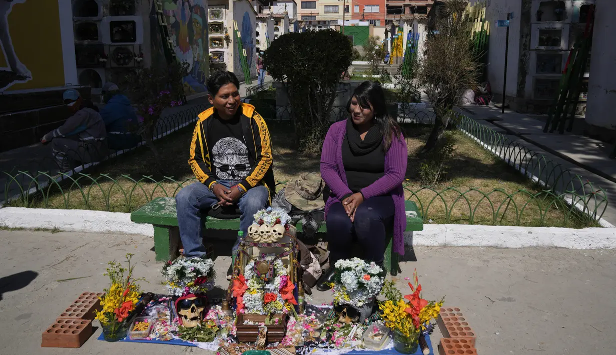Sepasang suami istri duduk dengan tengkorak manusia yang dihias untuk diberkati oleh seorang imam di Pemakaman Umum selama Festival Natitas di La Paz, Bolivia, Selasa (8/11/2022). Tradisi tahunan ini merayakan kematian di Bolivia dengan tengkorak yang dirawat dan didekorasi oleh mereka yang menggunakannya sebagai jimat untuk perlindungan. (AP Photo/Juan Karita)