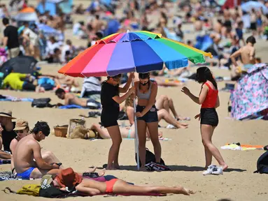Sejumlah wanita memasang payung saat menikmati cuaca hangat di Pantai St Kilda Melbourne, Australia (3/11/2020). Negara bagian Victoria di Australia mencatat nol kasus penularan COVID-19 selama empat hari berturut-turut setelah berjuang melawan gelombang kedua wabah pandemi. (AFP/William West)