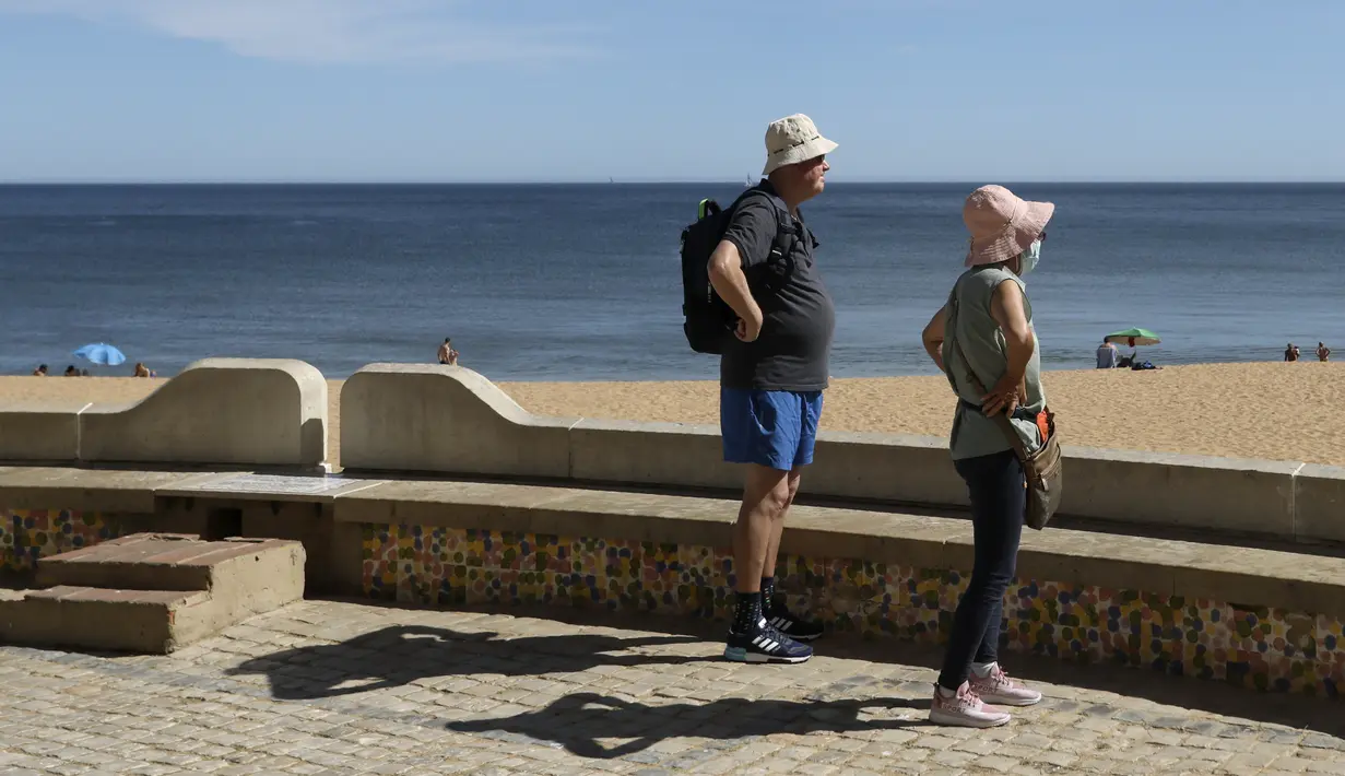 Sepasang turis melihat pantai di Albufeira, wilayah Algarve, Portugal, Senin (17/5/2021). Wisatawan Inggris mulai berdatangan dalam jumlah besar di bagian selatan Portugal pada hari Senin, setelah pemerintah di kedua negara melonggarkan pembatasan perjalanan pandemi COVID-19. (AP Photo/Ana Brigida)