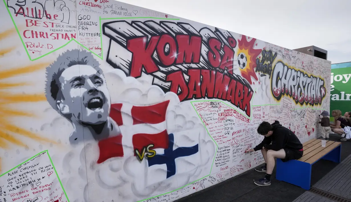 Orang-orang menulis harapan baik pada mural untuk gelandang timnas Denmark Christian Eriksen di dinding fanzone di Kopenhagen, Senin (14/6/2021). Eriksen mengalami serangan jantung dan sempat tak sadarkan diri saat memperkuat timnas Denmark vs Finlandia di Euro 2020. (AP Photo/Martin Meissner)
