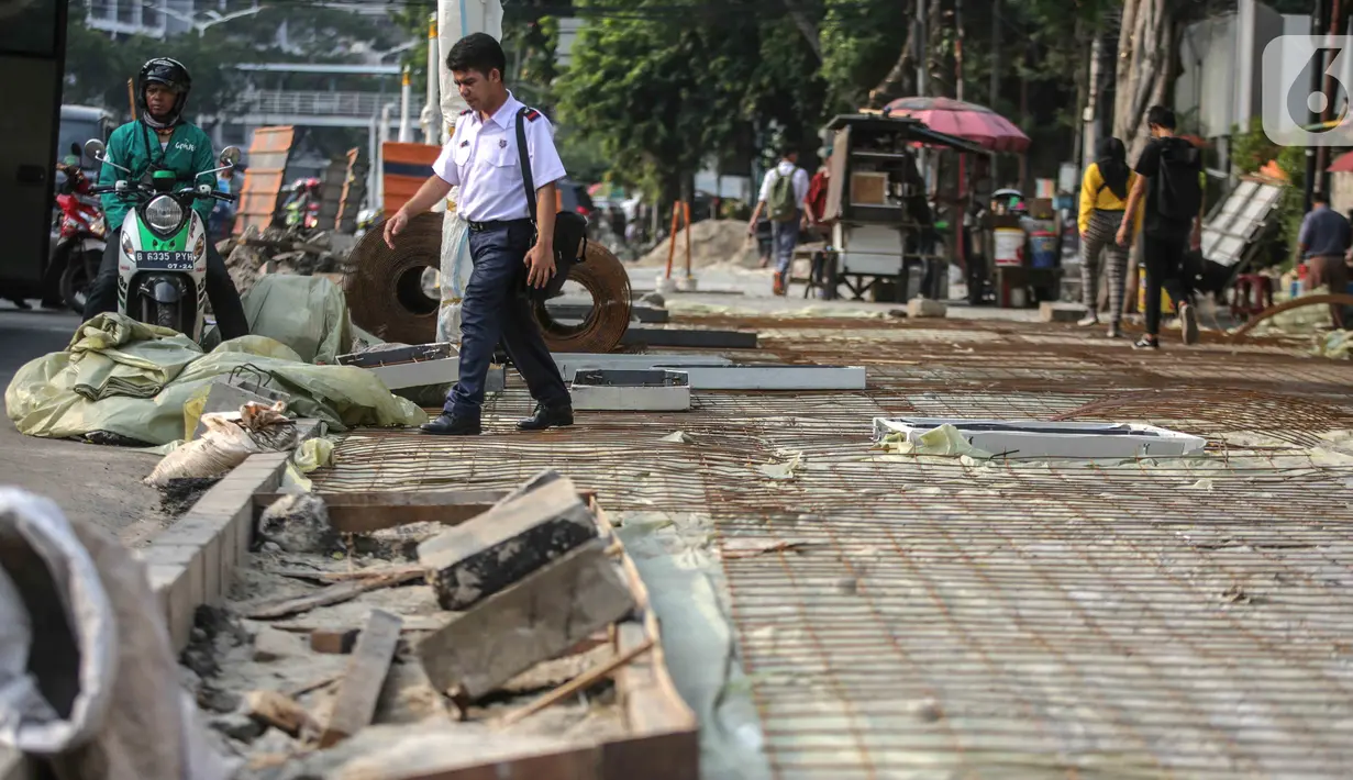Pejalan kaki melintasi trotoar yang sedang direvitalisasi di kawasan Kramat Raya, Jakarta, Rabu (6/11/2019). Revitalisasi trotoar menyebabkan para pejalan kaki harus berjalan di pinggir jalan dan bersinggungan dengan sepeda motor. (Liputan6.com/Faizal Fanani)
