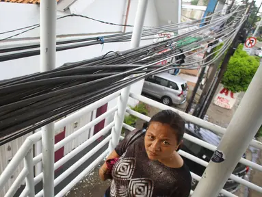 Warga melintas di bawah instalasi kabel yang menjuntai di JPO kawasan Cawang, Jakarta, Rabu (25/1). Selain mengganggu kenyamanan, buruknya penempatan instalasi kabel tersebut juga berbahaya bagi keselamatan pengguna JPO. (Liputan6.com/Immanuel Antonius)