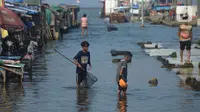 Anak-anak mencari ikan saat banjir rob di Pelabuhan Kali Adem, Muara Angke Jakarta, Rabu (5/1/2022). Menurut BMKG, adanya fase bulan baru yang bersamaan dengan masa Perigee (jarak terdekat bulan bumi) menyebabkan peningkatan signifikan ketinggian pasang air laut. (merdeka.com/Imam Buhori)