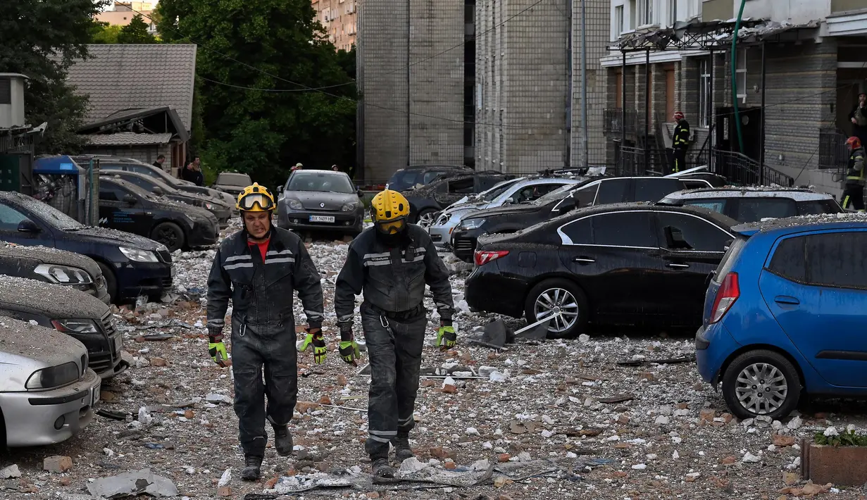 Tim penyelamat berjalan melewati mobil-mobil yang rusak di luar sebuah bangunan tempat tinggal bertingkat, yang sebagian hancur setelah serangan pesawat tak berawak pada malam hari di Kyiv pada 30 Mei 2023. (Sergei SUPINSKY/AFP)