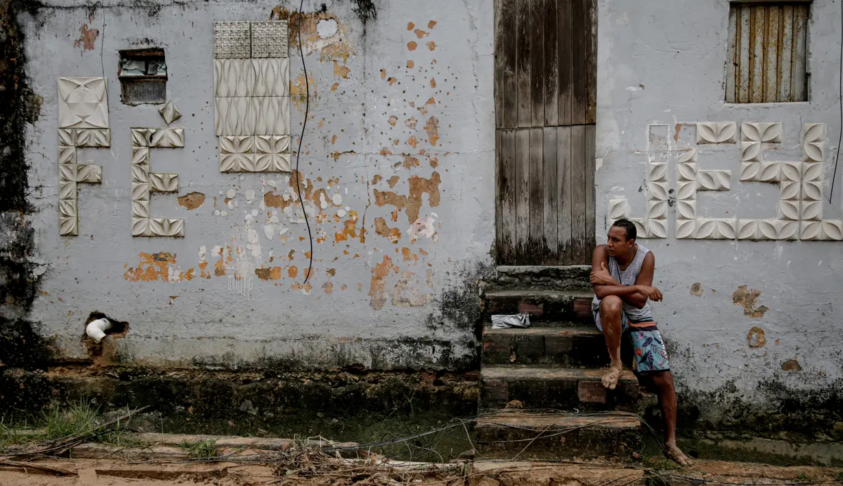 Seorang pria duduk di depan sebuah rumah yang rusak akibat tanah longsor pada malam hari di komunitas Jardim Monte Verde, lingkungan Ibura, di Recife, Negara Bagian Pernambuco, Brasil (29/5/2022). Hujan deras yang melanda negara bagian Pernambuco di timur laut Brasil menewaskan 34 orang. (AFP/Brenda Alcantara)