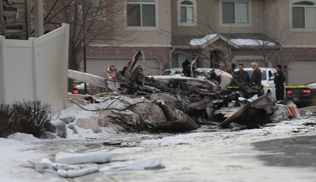 Petugas pemadam kebakaran dan penyelidik melihat puing-puing dari pesawat pribadi yang jatuh di kawasan perumahan Roy, Utah, Amerika Serikat, Rabu (15/1/2020). Pesawat menabrak atap rumah sebelum akhirnya menghantam tanah dan terbakar. (Ben Dorger/Standard-Examiner, via AP)
