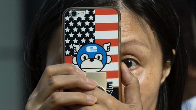 Seorang perempuan mengambil gambar dengan telepon yang memiliki sampul bertema bendera Amerika Serikat di luar Konsulat Amerika Serikat di Chengdu, China barat daya pada 26 Juli 2020. (AP Photo / Ng Han Guan)