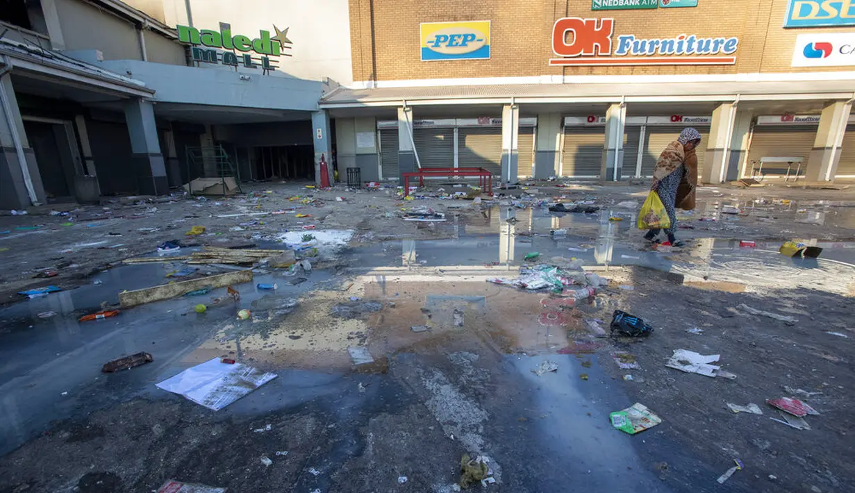 Seorang gadis muda membawa bahan makanan yang dijarah dari toko terdekat, berjalan pulang, di kompleks perbelanjaan Naledi di Vosloorus, timur Johannesburg, Senin (12/7/2021). Kerusuhan dan penjarahan yang dipicu penahanan mantan Presiden Afrika Selatan Jacob Zuma. (AP/Themba Hadebe)