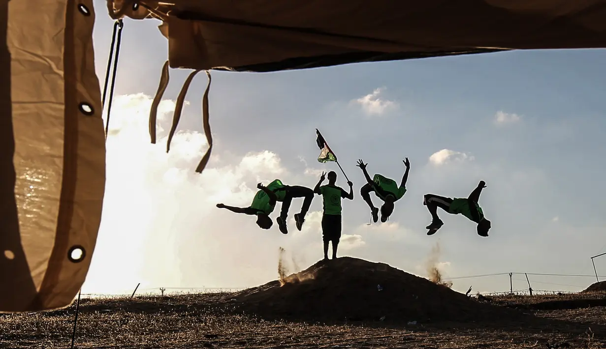 Empat pemuda Palestina mempraktekkan keterampilan parkour mereka di dekat tenda warga di perbatasan Gaza, Palestina (10/4). Mereka menghibur para warga yang melakukan aksi protes di perbatasan Gaza tersebut. (AFP Photo/Said Khatib)