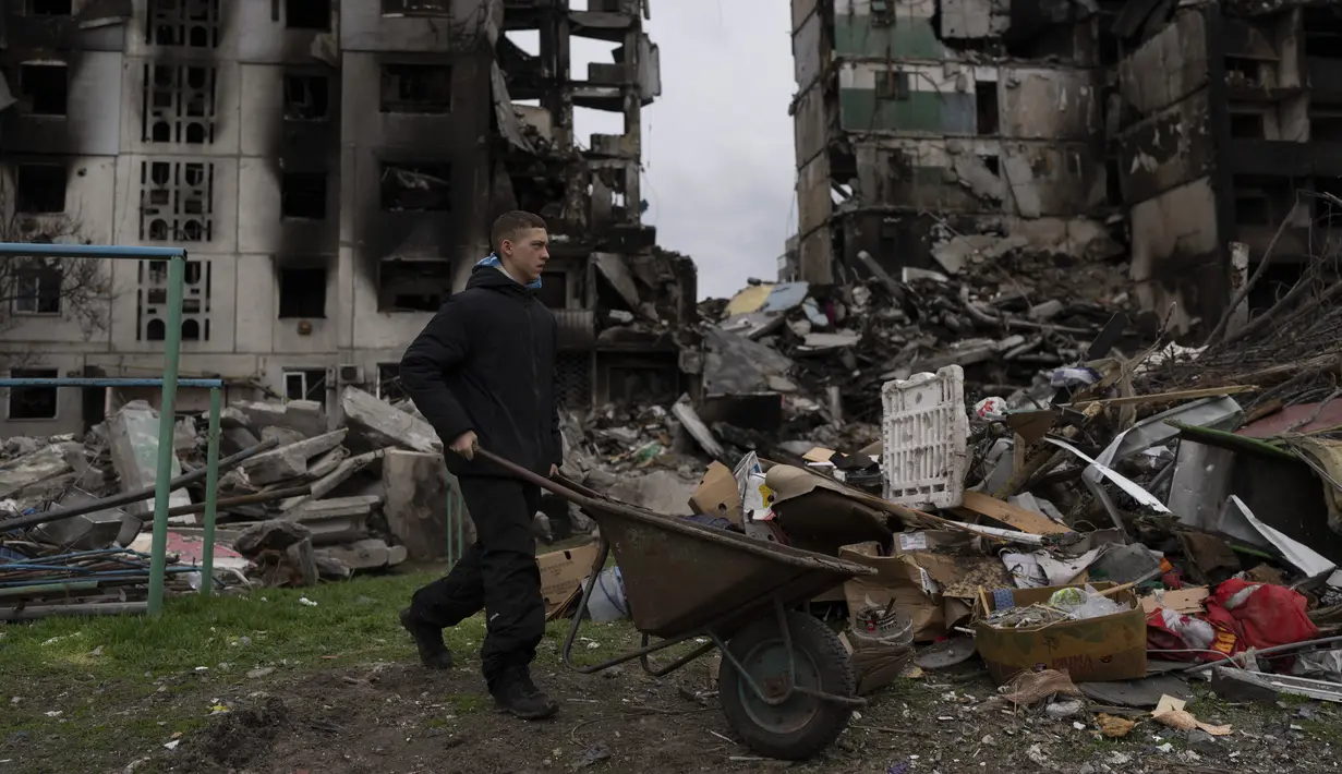 Seorang pemuda mendorong gerobak di depan gedung apartemen yang hancur di kota Borodyanka, Ukraina, pada Minggu, 10 April 2022. Invasi Rusia ke Ukraina hingga saat ini telah berlangsung selama 46 hari. (AP Photo/Petros Giannacouris)