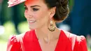 Kate tampak mengenakan gaun warna merah merona lansiran rumah mode favoritnya, Alexander McQueen dan topi bunga dari Philip Treacy.