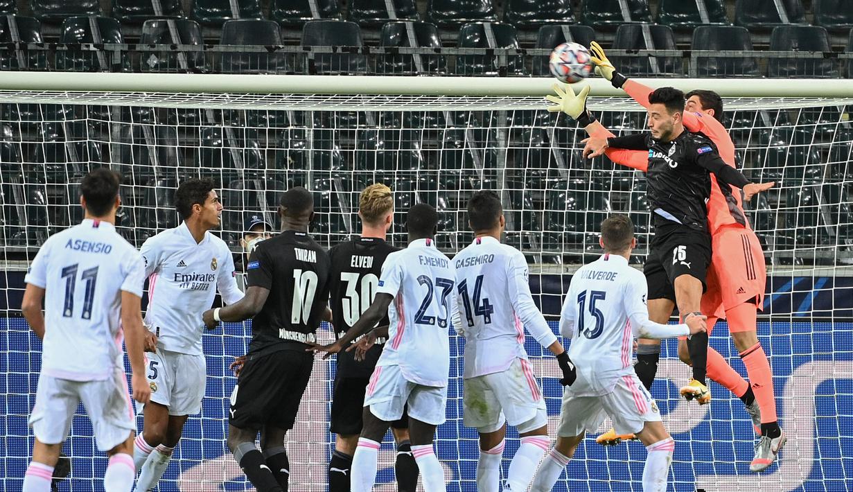 Kiper Real Madrid, Thibaut Courtois berusaha menangkap bola dari sundulan pemain Borussia Monchengladbach, Ramy Bensebaini  pada pertandingan grup B Liga Champions di  Borussia Park, Jerman, Selasa (27/10/2020). Madrid bermain imbang 2-2 atas Monchengladbach. (AFP Photo/Ina Fassbender)