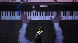 Seorang pria berjalan melewati layar yang menampilkan pianis Nobuyuki Tsujii bermain selama konser "The Pianist Special", bermain di dalam ruangan dan secara bersamaan disiarkan ke area terbuka pusat perbelanjaan di Tachikawa, Tokyo (11/4/2021). (AFP Photo/ Philip Fong)