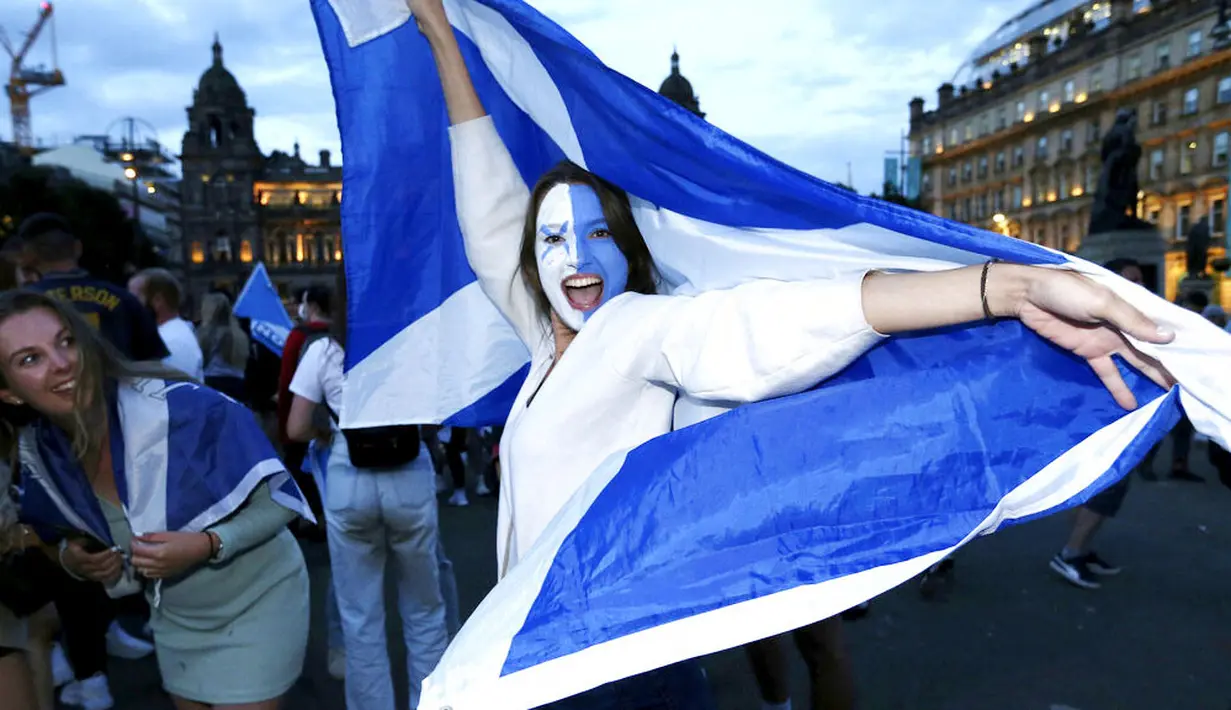 Seorang fans wanita menari sambil mengibarkan bendera Skotlandia saat merayakan hasil imbang melawan Inggris di Glasgow, Skotlandia, Jumat (18/6/2021). (Robert Perry/PA via AP)