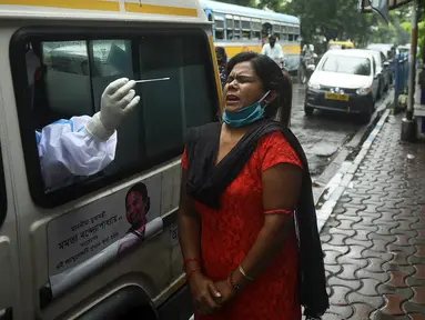 Seorang petugas kesehatan yang mengenakan alat pelindung diri (APD) mengambil sampel swab seorang wanita untuk menguji virus corona Covid-19, dari ambulans di depan pasar kota, di Kolkata (1/9/2020). (AFP/Dibyangshu Sarkar)