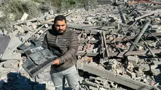 Seorang pria memegang rompi rusak bertuliskan “Press” di tengah puing-puing lokasi serangan udara Israel yang menargetkan area di mana sejumlah wartawan berada di desa Hasbaya, Lebanon selatan, pada Jumat 25 Oktober 2024. (Ali Hankir/AFP)