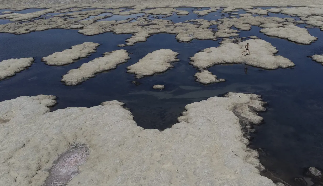 Olof Wood berjalan melintasi struktur mirip karang yang disebut mikroba, yang tersingkap oleh air yang surut di Great Salt Lake (6/9/2022). Gelombang panas terik memecahkan rekor di Utah, di mana suhu mencapai 105 derajat Fahrenheit (40,5 derajat Celcius) pada hari Selasa, menjadikannya hari terpanas September yang tercatat sejak tahun 1874. (AP Photo/Rick Bowmer)