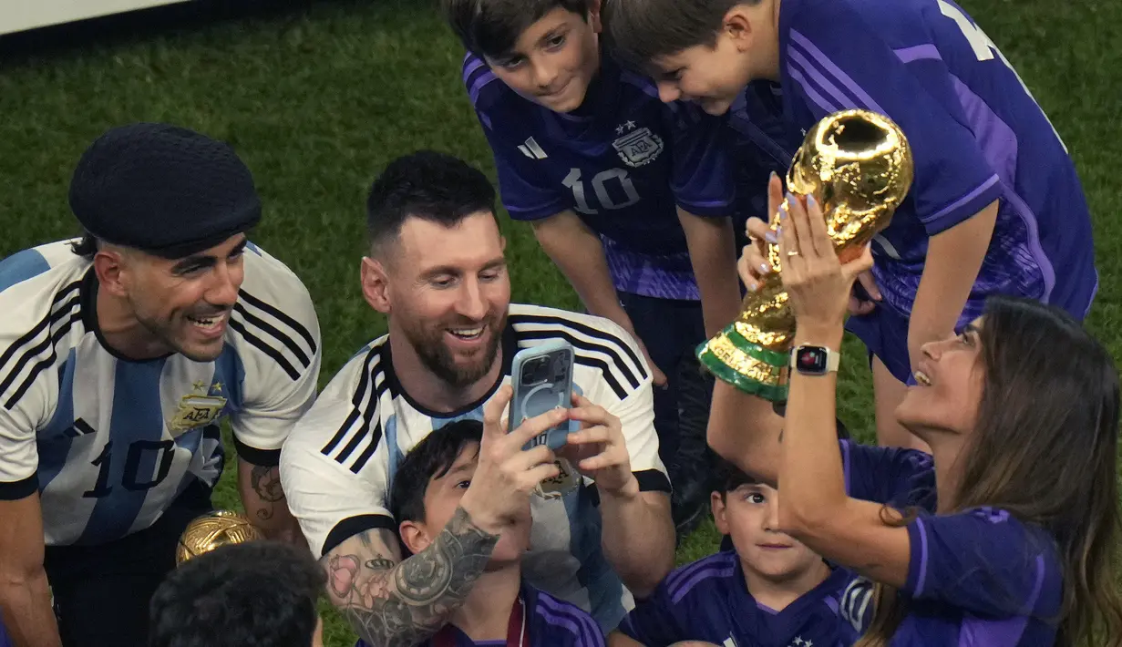 Pemain Argentina, Lionel Messi memotret istrinya, Antonela Ruccuzzo (kanan) yang sedang memegang trofi Piala Dunia 2022 setelah timnya berhasil mengalahkan Prancis pada laga final yang berlangsung di Lusail Stadium, Qatar, Minggu (18/12/2022). Albiceleste menang 4-2 atas Prancis di babak penalti. (AFP/Jewel Samad)